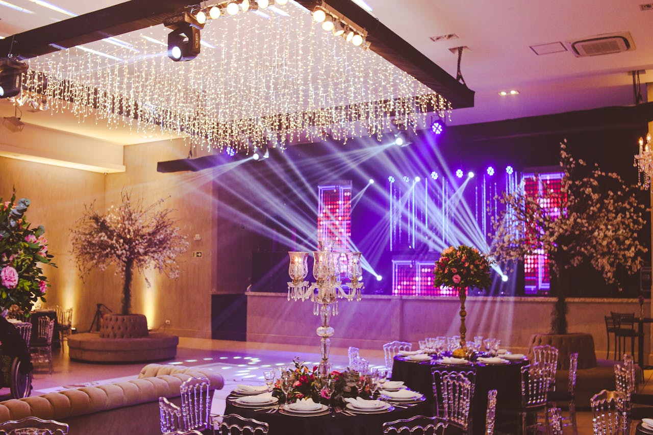 why-choose-us Stunning ballroom setup decorated with crystal chandeliers, floral arrangements, and vibrant stage lighting.