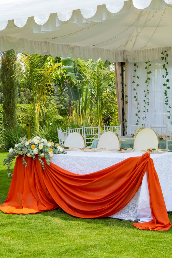 hero-img-01 Beautifully decorated outdoor wedding table with orange drapery and green surroundings.