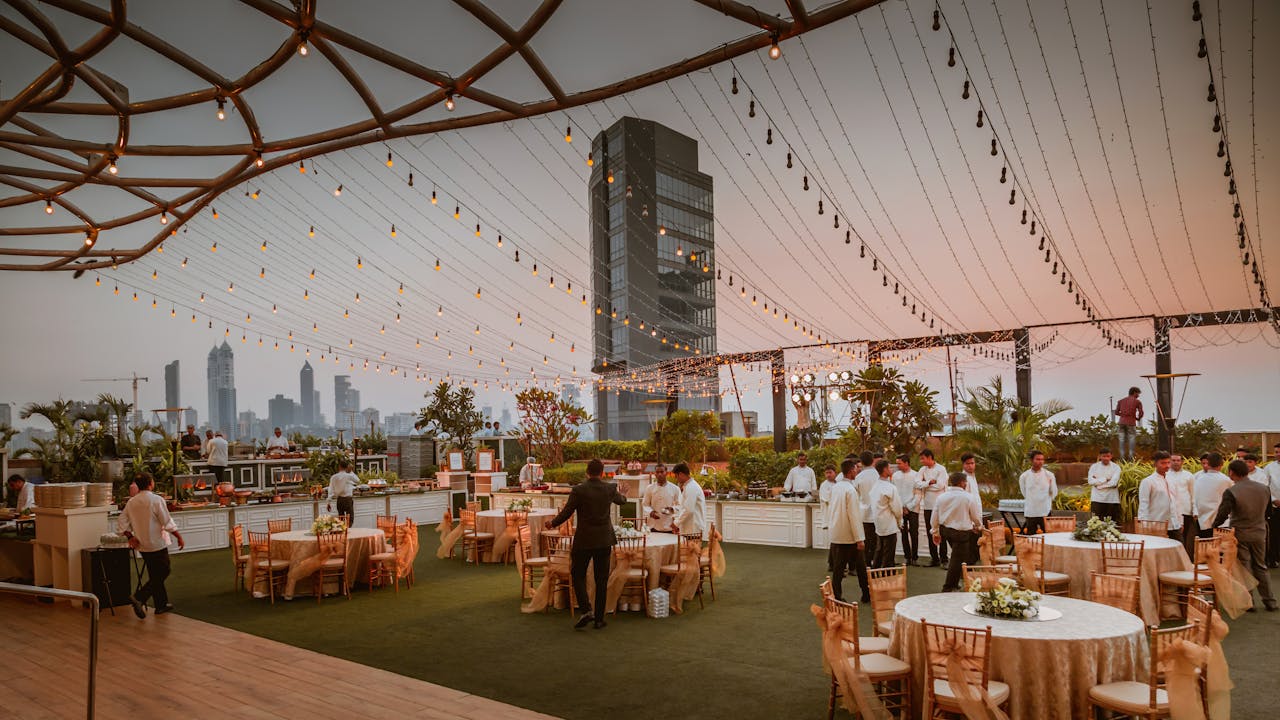 services-01 Elegant rooftop event with tables and lights set against Mumbai skyline at sunset, India.