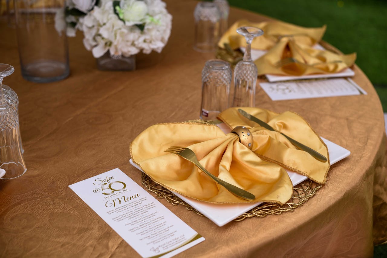 services-03 A luxurious gold-themed table setting with menu, napkins, and crystal glassware for a 50th anniversary celebration.
